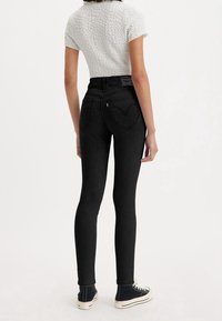Jean skinny noir taille haute avec une texture lisse et des poches arrière en forme de cœur. Associé à un haut blanc à manches courtes texturé et des baskets noires.