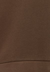 Gros plan d'un tissu en coton marron avec une couture près du bas, montrant une texture lisse et des détails de couture fins.