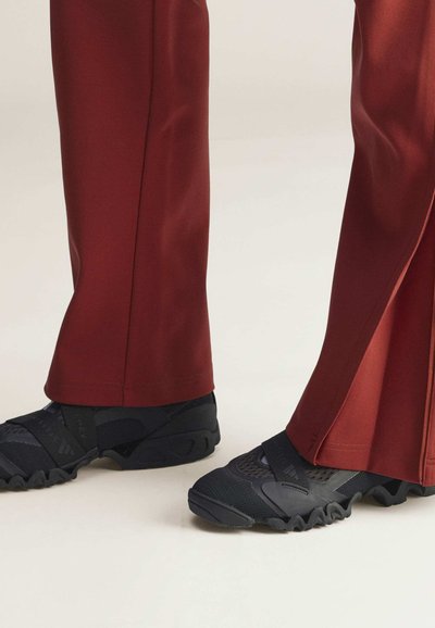 Donkerrode sportbroek met een rechte pijp en een zijsplit; gecombineerd met zwarte sneakers met een gestructureerd oppervlak en kruisbanden.