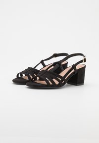 Sandali con tacco in camoscio nero, dotati di tacco a blocco, con design a cinturini incrociati e cinturino alla caviglia regolabile con dettagli in metallo dorato.