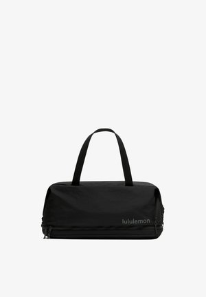 Melns Lululemon ceļojuma soma ar divām rokturiem un nodalījumiem ar rāvējslēdzējiem, izstrādāta daudzveidīgai lietošanai un vieglai pārnestei.