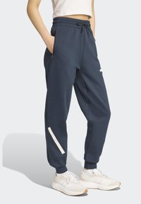 Námornícke modré tepláky s elastickým pásom, bočnými vreckami a bielymi akcentmi na dolnej časti nohavíc. Vyrobené z jemnej, texturovanej látky.