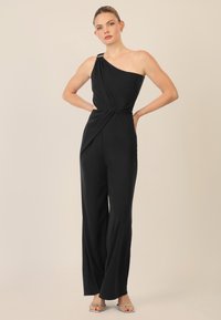 Mono negro de un solo hombro con cintura retorcida. Hecho de una tela suave, presenta una silueta elegante y mínimos acentos de hardware.