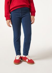 Jeans de mezclilla azul con un ajuste slim, que cuentan con una textura suave y una cintura de altura media, combinados con zapatillas rojas con acentos blancos.