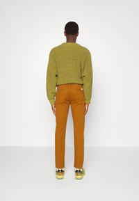 Pull tricoté vert olive, coupe ample ; pantalon marron avec jambes droites ; chaussures au design coloré et texturé avec des accents.