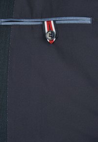 Navy-Stoff mit glatter Textur zeigt einen Knopf mit einem rot-weiß-blauen Streifenakzent und einem kontrastierenden blauen Saum darüber.