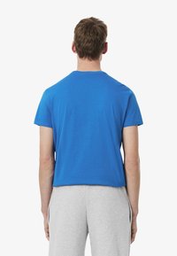 Camiseta de algodón azul con mangas cortas y escote redondo, vista desde la parte de atrás, combinada con pantalones deportivos grises. Diseño simple y sin adornos.