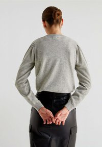 Szary sweter dzianinowy z długimi rękawami i detalami w postaci falbanek, w połączeniu z czarną skórzaną spódnicą z kieszeniami. Prezentujący gładką fakturę.