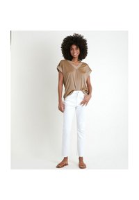 Top bronzo a V con maniche corte, jeans bianchi dritti e sandali marroni. Il top ha una texture scintillante e una vestibilità rilassata.