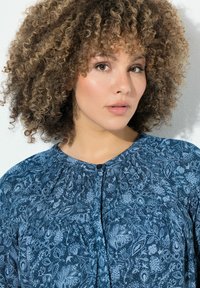 Blusa fluida blu con motivo floreale, scollo plissettato e chiusura a bottoni frontale. Realizzata in tessuto leggero con una consistenza morbida.