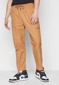 Beiga cargobyxor med resårlinning och dragsko, avsmalnande passform, sidoficka och slät bomullstyg. Bärs med svartvita sneakers.