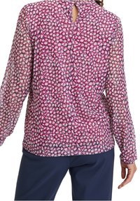 Blouse met lange mouwen van doorschijnende, roze stof met cirkelpatronen en een sleutelgatdetail aan de achterkant, gecombineerd met donkerblauwe broek.