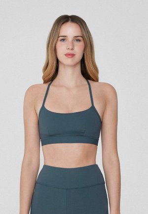 Bra de sport en vert émeraude foncé avec des fines bretelles réglables, une large bande et un tissu lisse. Conçu pour le confort et le soutien pendant les activités.