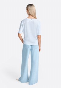 Haut à manches courtes rayé bleu clair avec un col rond et un petit logo. Associé à un jean large bleu clair, au toucher lisse et à la coupe décontractée.