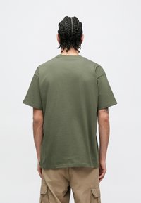 Olívazöld pamut póló laza fazonnal, rövid ujjakkal és kerek nyakkivágással. Sima textúra, minta vagy látható díszítés nélkül.