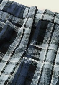 Rudemønstret stof i nuancer af sort, marineblå og lyseblå. Teksturvævning med kontrasterende tern og en lynlåsdetalje ved livlinjen.