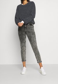 Mörkgrå stickad tröja med ribbad struktur, kombinerad med högmidjade ljusgrå slitna jeans och vita sneakers.