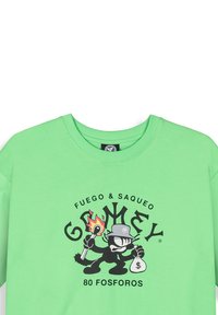 Camiseta de algodón verde con un estampado gráfico de un personaje de dibujos animados sosteniendo fuego y una bolsa de dinero, con elementos de texto y diseño de logo.