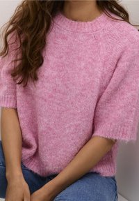 Maglione rosa a maglia testurizzata con maniche corte e scollatura ampia. Materiale morbido con un aspetto soffice, indossato in modo sciolto sopra dei jeans blu.