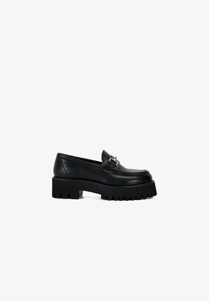Mocassin à plateforme en cuir noir avec semelle crantée épaisse et petit détail de boucle dorée sur le devant supérieur.