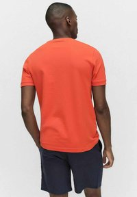 Kortärmad t-shirt i klar orange bomull, med rund hals och regular fit. Bärs med marina shorts. Bakifrån visad.