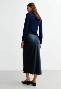 Haut en tricot bleu marine à manches longues associé à une jupe satin lisse de longueur au sol dans une teinte de bleu plus foncé. Chaussures plates noires.