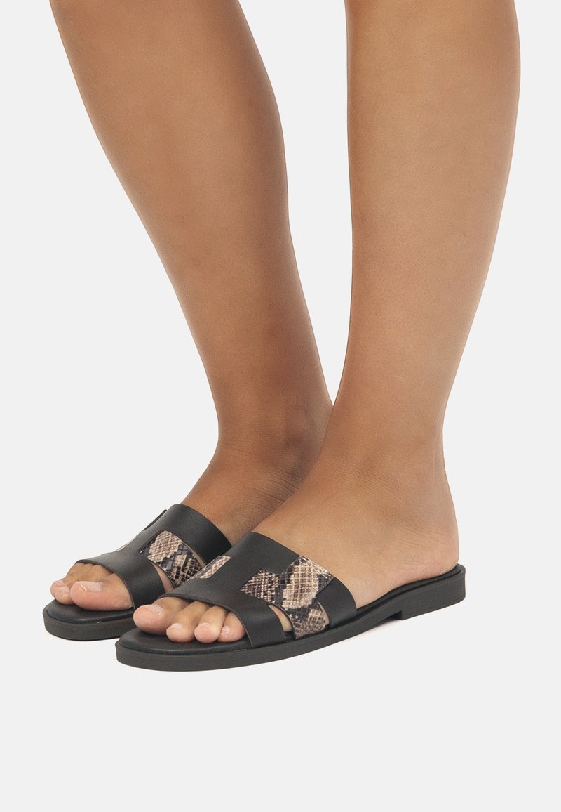 Chanclas negras de slide con banda texturizada de estampado de serpiente. Diseño de punta abierta y suela plana, que presenta cuero suave y acentos estampados.