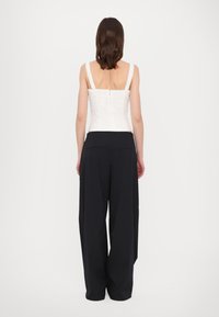 White lace corset top with wide straps, paired with loose-fitting black trousers. Trousers feature a tailored design and back pockets.