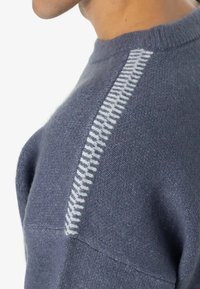 Mezgimo megztinis tamsiai mėlynos spalvos su tekstūruota balta juostele per petį. Minkšta medžiaga ir apvalus kaklas.