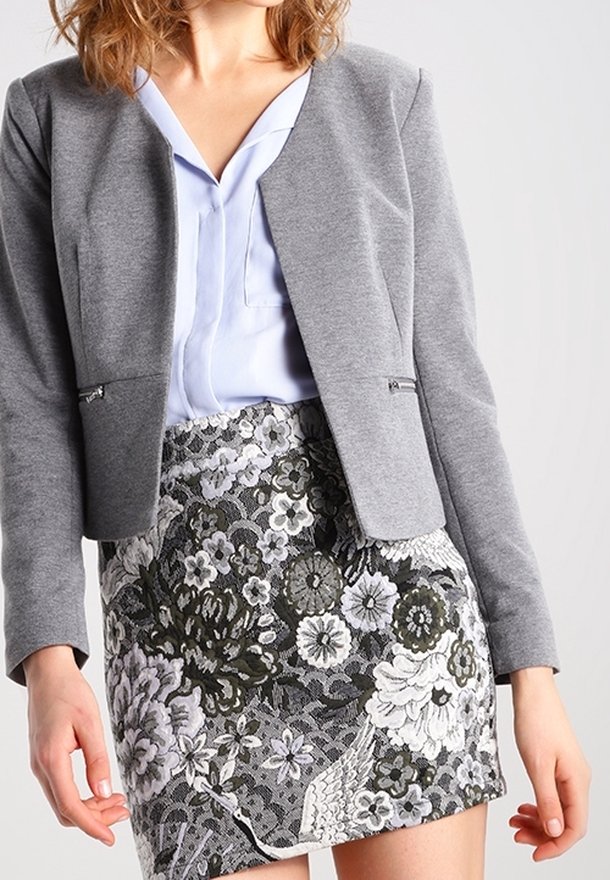Femme portant un chemisier bleu clair, un blazer gris court et une jupe à motif floral noir et blanc.