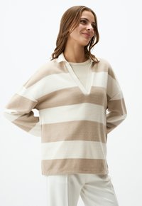 Maglione a righe beige e crema con scollo a V e maniche lunghe, realizzato in morbido materiale a maglia. Presenta un colletto bianco e un design a vestibilità ampia.