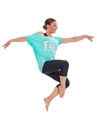 En ljusblå, lös t-shirt med vit text, ihop med svarta korta leggings. Motivet är i ett mellansteg av ett hopp, barfota.