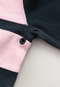 Dunkelblaues und hellrosa Baumwollstoff mit einem Farbblockdesign. Zwei Druckknöpfe an der Kante sichtbar, glatte Textur.