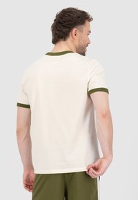 T-shirt in cotone crema con colletto e polsini a coste verde scuro. Design semplice, forma aderente e texture liscia.