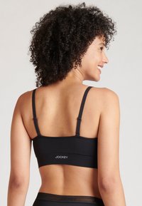 Svart stretchtygsbh med tunna justerbara axelband, som har en slät, sömlös design och en diskret logotyp på baksidan.