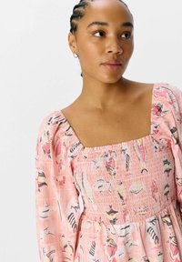 Vestido rosa con mangas abullonadas y escote cuadrado. Presenta un corpete fruncido y un divertido patrón de peces en varios colores. Textura de tela suave.