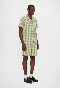 Πράσινο και λευκό καρό κοντομάνικο πουκάμισο και ταιριαστές βερμούδες. Διαθέτει γιακά, τσέπες patch και άνετη εφαρμογή. Φοριέται με μαύρα παπούτσια.