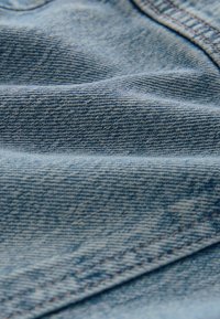 Világoskék denim anyag sima textúrával, amely átlós szövést és finom eltéréseket mutat. Látható varrott szélek.