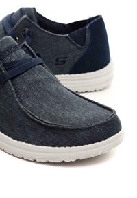 Scarpe in denim navy con texture liscia, suola in gomma bianca e lacci elastici. Presentano un tacco parziale e un accento del logo sul lato.