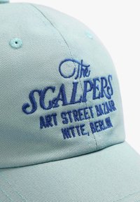 Hellblaues Baumwollcap mit gebogenem Schirm, versehen mit blauer gestickter Schrift: "Der SCALPERS ART STREET BAZAAR HITTE, BERLIN."