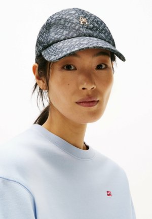 Denim-mønstret baseballcap med en buet skygge, der har et metallic logo, båret sammen med en lyseblå sweatshirt.