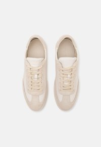 Sneaker beige con tomaia in suede e pelle, lacci piatti, lingua imbottita e logo in rilievo. Texture liscia con design a punta tonda.