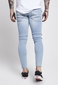 Jeans ajustados de denim azul claro con una textura suave, que cuentan con bolsillos traseros y un ajuste ceñido. Combinados con zapatillas negras Vans.
