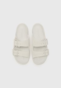 Lys grå sandaler med to justerbare spenner, mykt skinnoverdel, åpen tå-design, flat såle og subtil merking på innersålen.