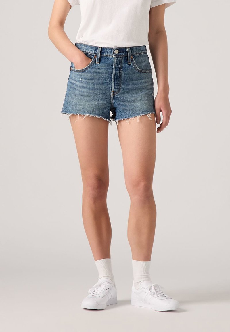 Shorts in denim con bordo sfrangiato, lavaggio azzurro chiaro, design a cinque tasche e chiusura con bottoni. Abbinati a sneaker bianche e calzini.