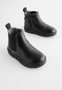 Bottines en cuir noir avec doublure en polaire grise, panneaux élastiques sur les côtés et fermeture éclair sur le côté. Détails cousus le long de la semelle.