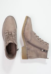 Hnědé semišové kotníkové boty s šněrováním, bočním zipem a texturovanou gumovou podrážkou. Zpevněné švy podél okrajů.