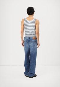Gestreepte tanktop, ruime blauwe jeans met een rafelrand, twee achterzakken, label op de tailleband, zwarte schoenen, bekeken van achteren.