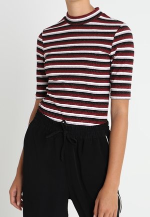 Haut côtelé rayé rouge, noir et blanc avec un col montant et des manches à mi-longueur, associé à un pantalon noir à taille élastique.