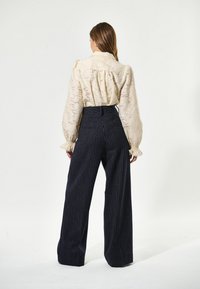 Blusa in tessuto pesca con maniche a sbuffo, abbinata a pantaloni navy a vita alta con sottili righe verticali e tasche posteriori.